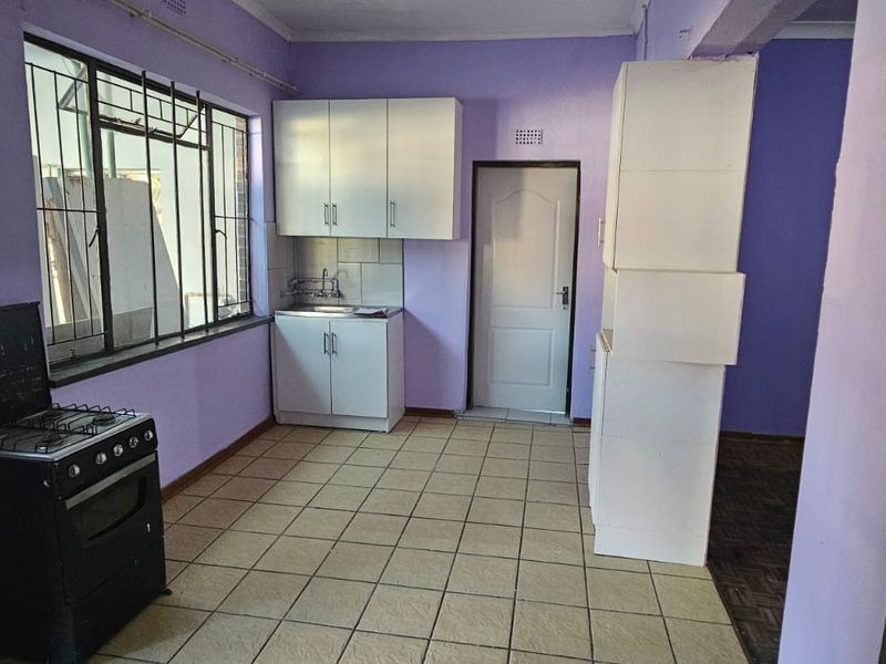 A basic kitchen area featuring tiled flooring, built-in cabinetry, a stainless steel sink, and security bars on the windows.