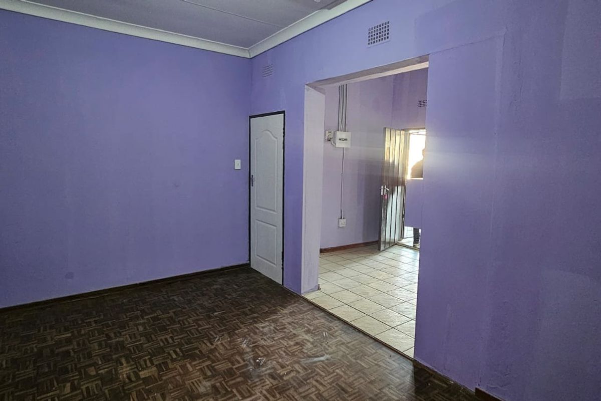 An empty living area featuring parquet flooring and coved ceilings, leading into an adjacent tiled space with a security gate.