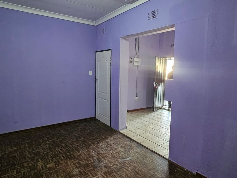 An empty living area featuring parquet flooring and coved ceilings, leading into an adjacent tiled space with a security gate.