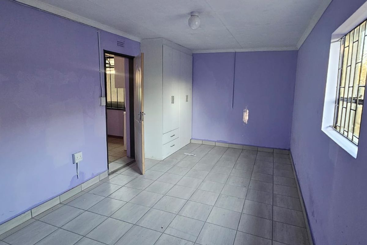 An empty bedroom featuring tiled flooring, built-in cupboards, and security bars on the window, ready for personalization.