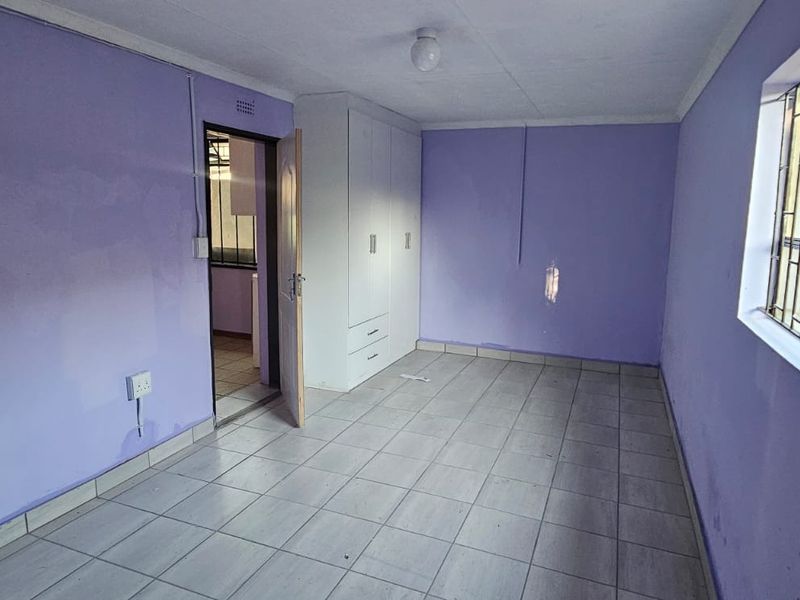 An empty bedroom featuring tiled flooring, built-in cupboards, and security bars on the window, ready for personalization.