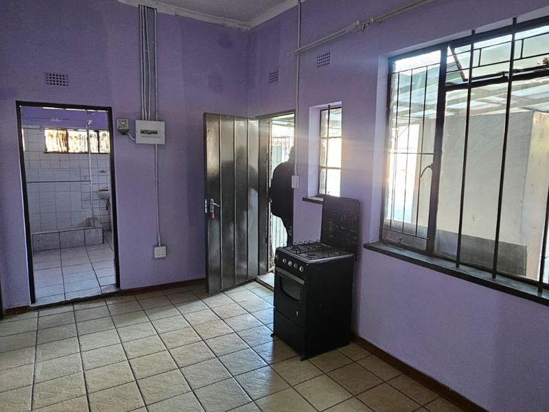 A functional kitchen area featuring tiled flooring, a freestanding stove, and direct access to an adjacent bathroom and exterior space.