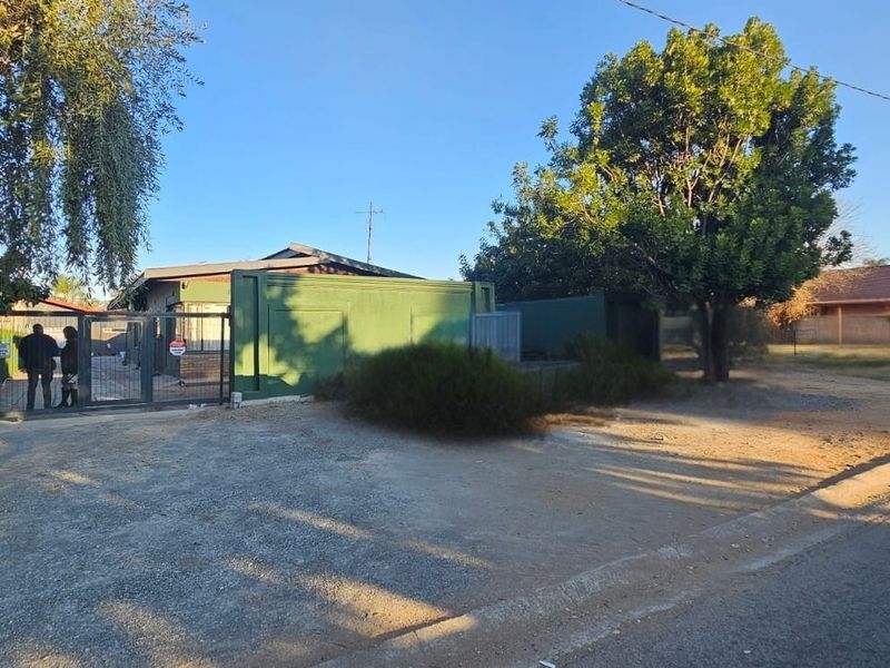 Front exterior view of the property featuring a metal security gate, perimeter wall, and an unpaved gravel driveway area.