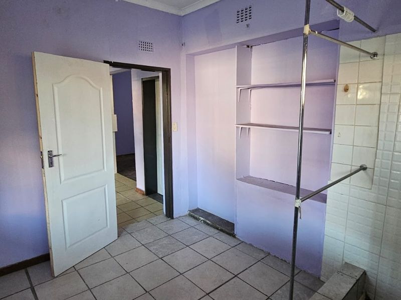 A functional bathroom space featuring a tiled shower enclosure, built-in wall shelving, and tiled flooring, ready for modernization and cosmetic updates.