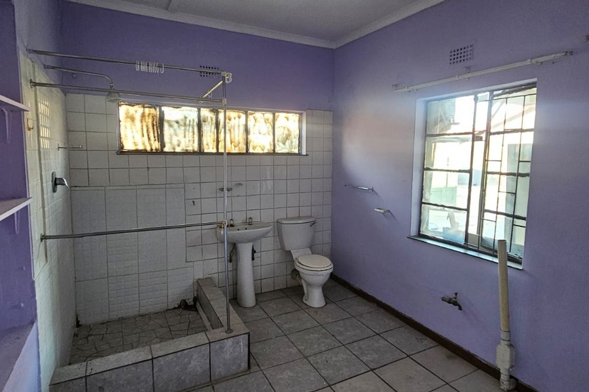 A dated bathroom featuring a pedestal basin, toilet, and shower enclosure with tiled walls and flooring, requiring cosmetic updates.