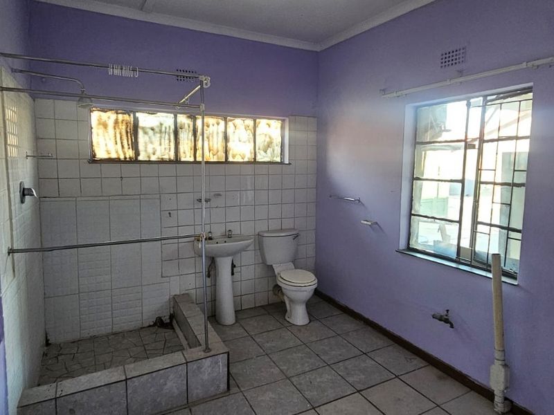 A dated bathroom featuring a pedestal basin, toilet, and shower enclosure with tiled walls and flooring, requiring cosmetic updates.
