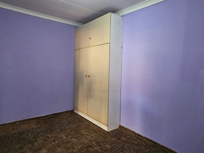 An empty bedroom featuring parquet flooring, coving, and a built-in cupboard, offering a blank canvas for renovation and interior design updates.