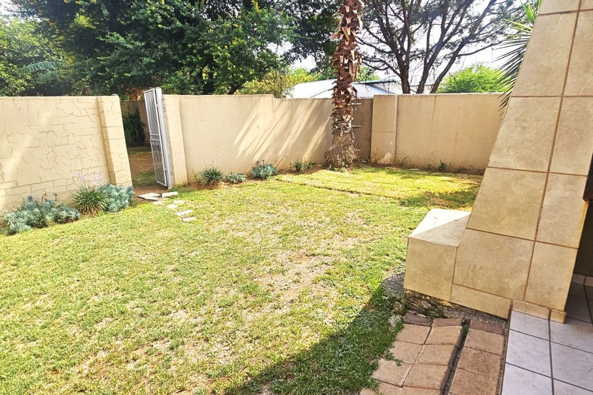 A private rear garden featuring a lawn, perimeter wall, and a built-in braai area with a tiled patio.