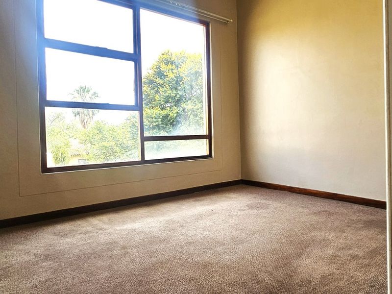 An empty bedroom featuring large windows that provide natural light, carpeted flooring, and neutral wall finishes, ready for personalization.