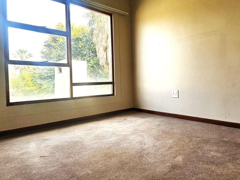 An empty bedroom featuring carpeted flooring, a large window providing natural light, and standard electrical fixtures.