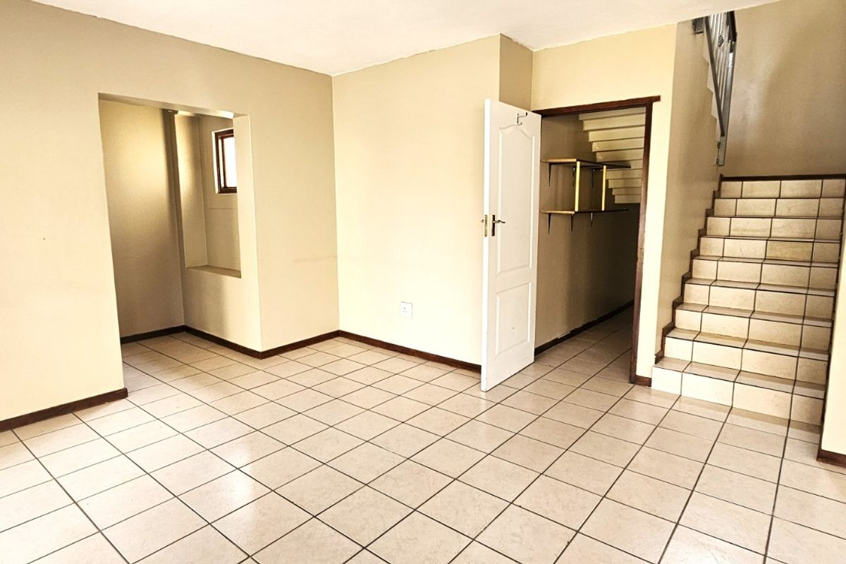 An empty living area featuring tiled flooring, a staircase, and access to adjacent rooms, presenting a blank canvas for interior design.