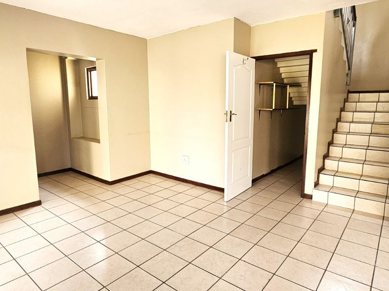 An empty living area featuring tiled flooring, a staircase, and access to adjacent rooms, presenting a blank canvas for interior design.