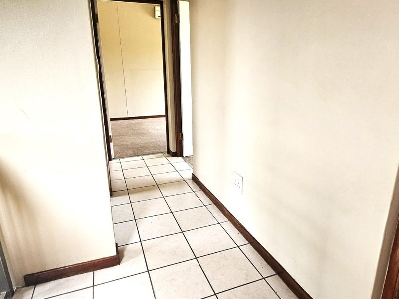 A bright, tiled hallway featuring a timber handrail and metal balustrade, leading to an adjacent bedroom area.