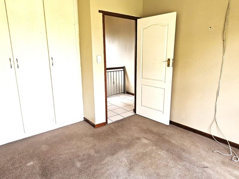 An empty bedroom featuring built-in cupboards, carpeted flooring, and access to a hallway, requiring minor cosmetic updates and repairs.
