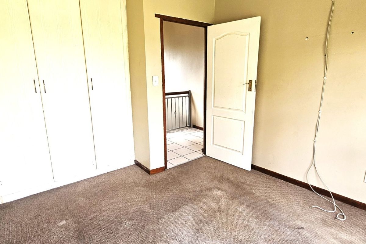 An empty bedroom featuring built-in cupboards, carpeted flooring, and access to a hallway, requiring minor cosmetic updates and repairs.