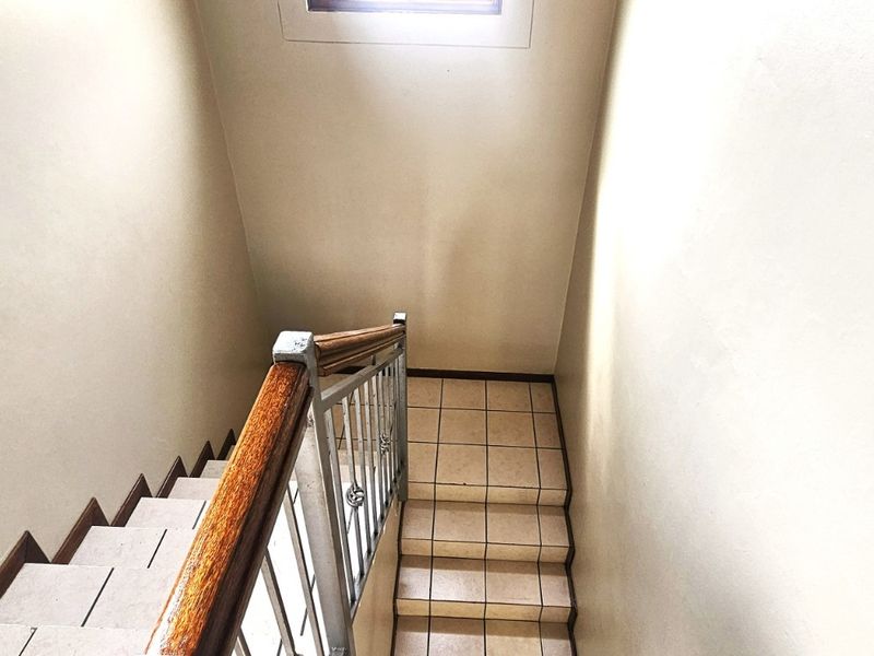 A functional staircase featuring tiled steps, a wooden handrail, and a metal balustrade, providing access between levels in the townhouse.
