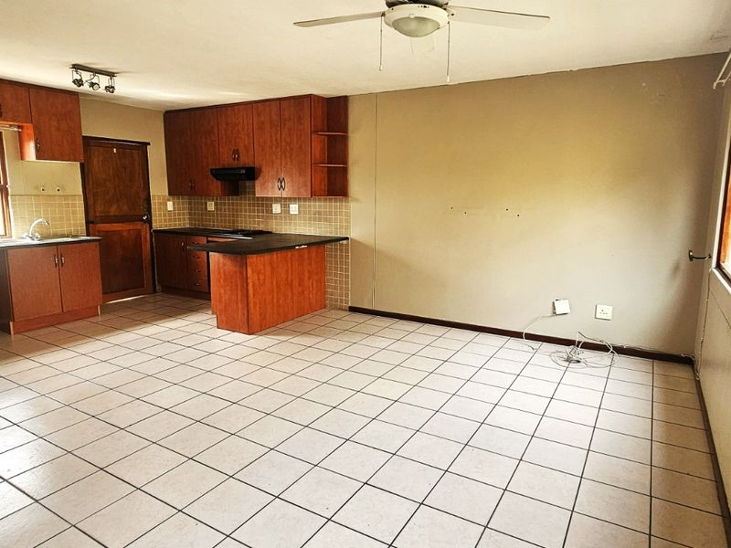Spacious open-plan kitchen and living area featuring tiled floors, wooden cabinetry, and built-in appliances, offering a functional layout ready for modernization.