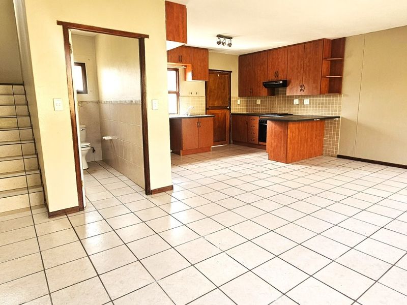 Open-plan living area featuring tiled flooring, a staircase, and a functional kitchen with built-in cabinetry, plus an adjacent guest toilet.