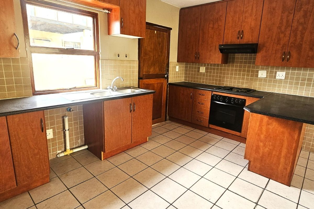 A functional kitchen featuring wooden cabinetry, laminate countertops, built-in oven, hob, and tiled flooring, offering a practical layout for renovation.