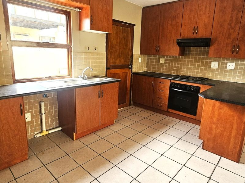 A functional kitchen featuring wooden cabinetry, laminate countertops, built-in oven, hob, and tiled flooring, offering a practical layout for renovation.