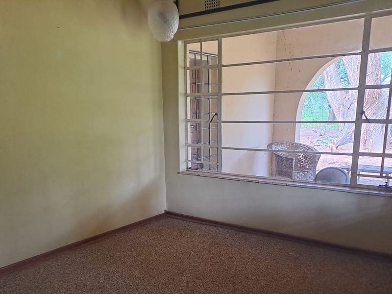 An empty living room featuring carpet flooring, a large window with security bars, and views of the outdoor area.