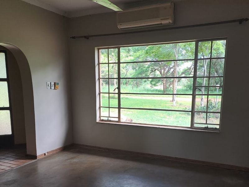 An empty living room featuring an arched entryway, large window with garden views, and a wall-mounted air conditioning unit.