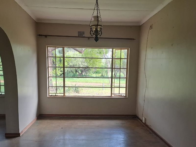 An empty living room featuring large steel-framed windows, an arched entryway, and a classic pendant light fixture, offering a bright and open space.