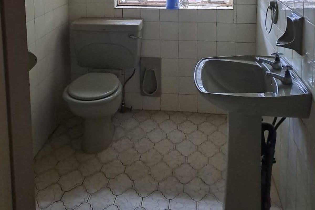 A dated bathroom featuring a pedestal basin and toilet with original wall and floor tiling, requiring modernization and cosmetic updates.