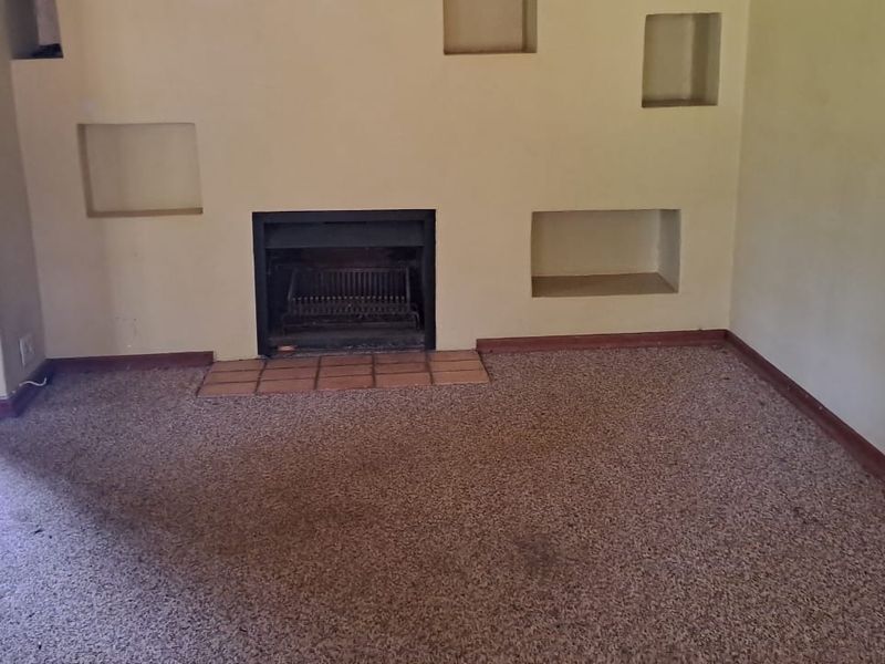 An empty living room featuring a built-in fireplace with a tiled hearth and decorative recessed wall niches.