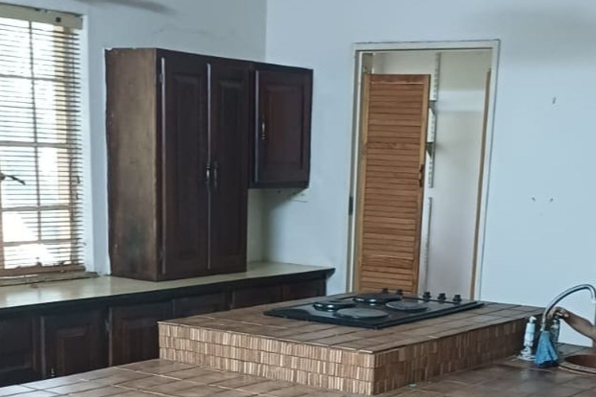 A dated kitchen featuring dark wood cabinetry, a tiled island with a built-in hob, and a separate pantry area with a louvered door.