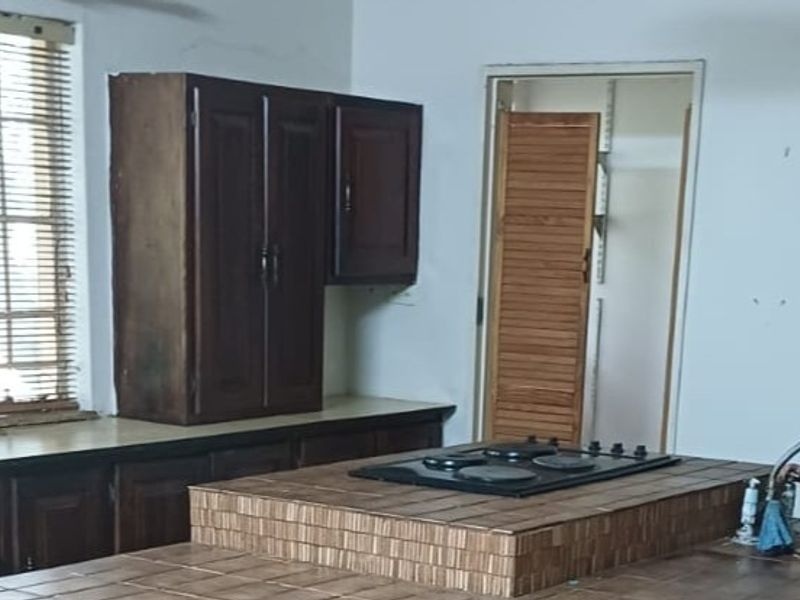 A dated kitchen featuring dark wood cabinetry, a tiled island with a built-in hob, and a separate pantry area with a louvered door.