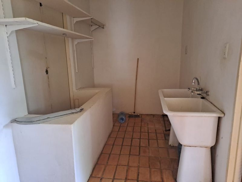 A functional laundry area featuring a double basin utility sink, wall-mounted shelving, and tiled flooring, offering a practical space for utility tasks.