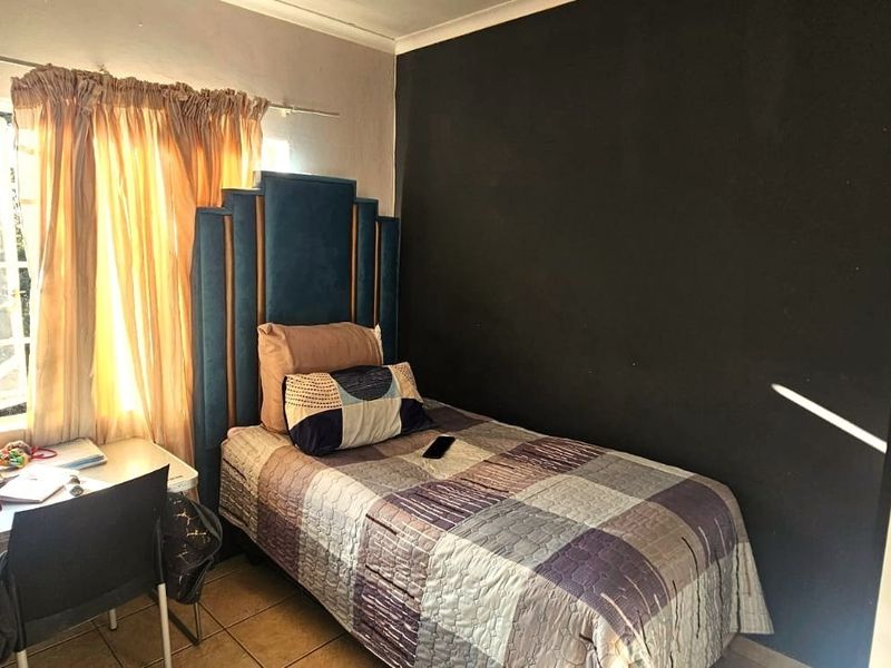 A compact bedroom featuring tiled flooring and a window with security bars, finished with a dark accent wall.