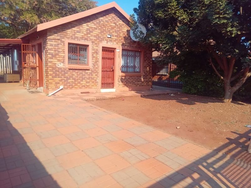 Rear view of a face brick house featuring a paved patio area and security fixtures on windows and doors.