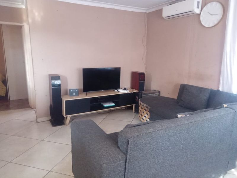 A living room featuring ceramic floor tiles, a wall-mounted air conditioning unit, and coved ceiling cornices.