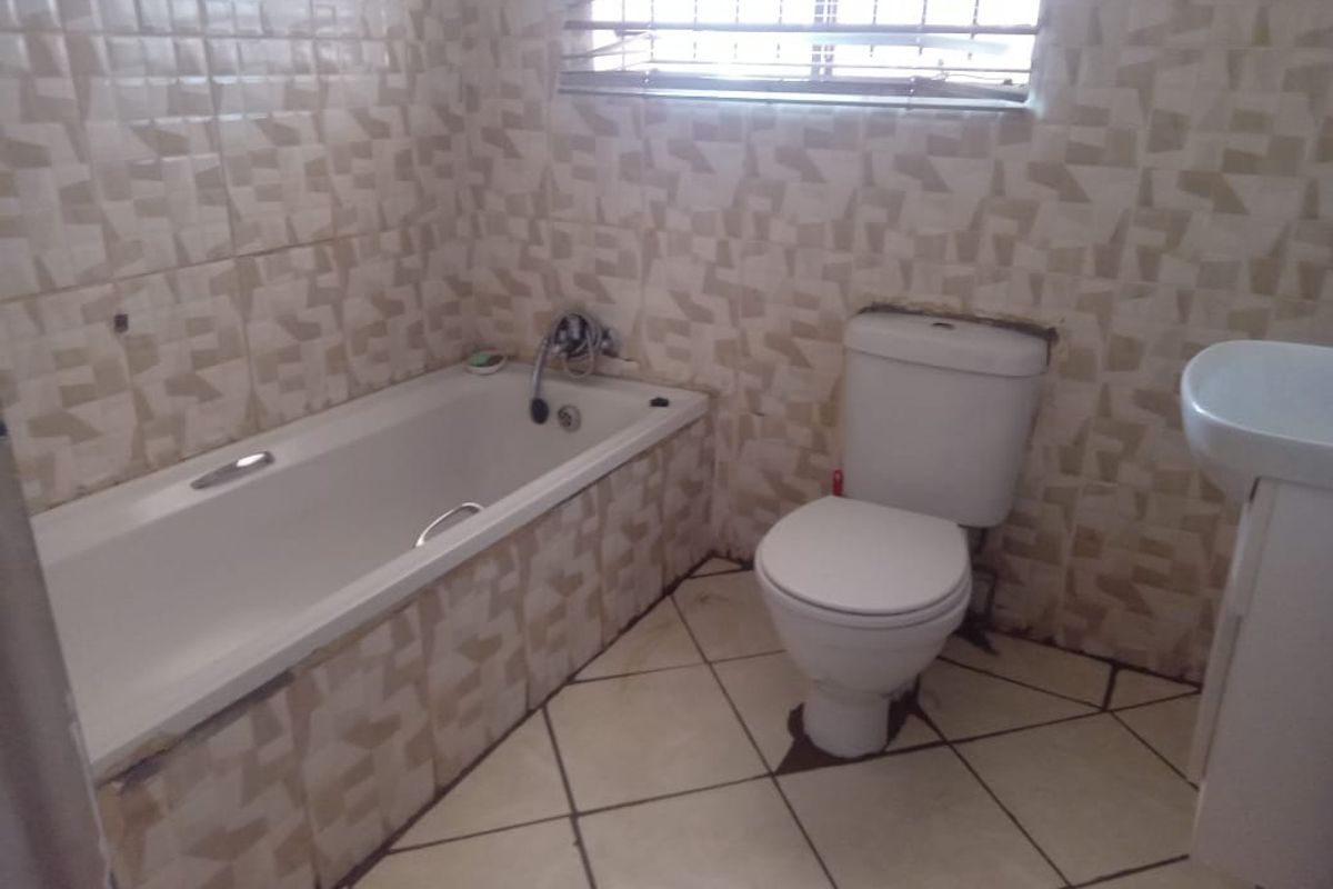 A functional bathroom featuring a bathtub, toilet, and pedestal basin with tiled finishes throughout, requiring some maintenance and cosmetic updates.