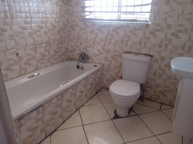 A functional bathroom featuring a bathtub, toilet, and pedestal basin with tiled finishes throughout, requiring some maintenance and cosmetic updates.