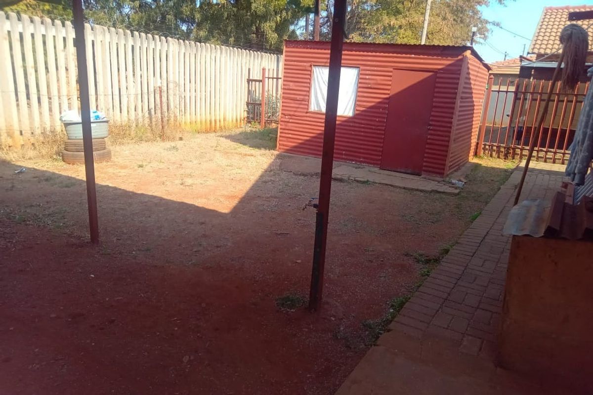 A rear yard area featuring a corrugated metal shed, paved walkway, and perimeter fencing, offering potential for landscaping and outdoor improvement.