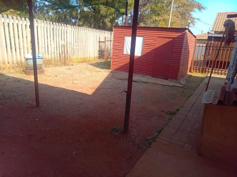 A rear yard area featuring a corrugated metal shed, paved walkway, and perimeter fencing, offering potential for landscaping and outdoor improvement.