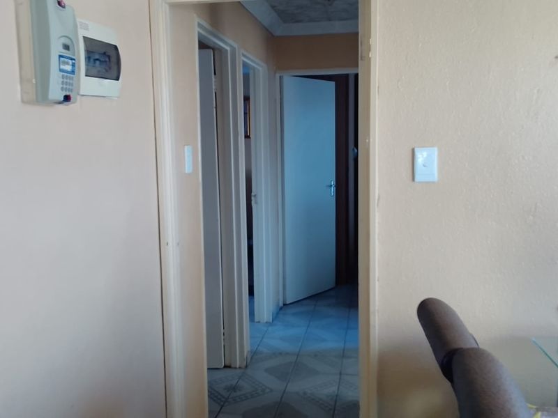 A functional hallway connecting multiple rooms, featuring tiled flooring, an alarm system keypad, and an electrical distribution board.