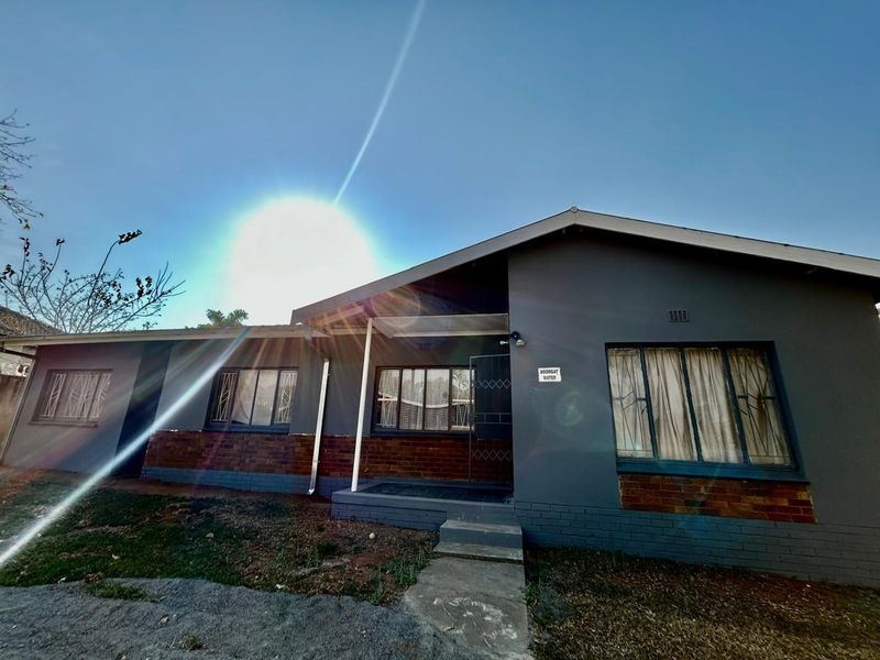Front elevation of a single-story house featuring a painted brick facade, security window bars, and a concrete entrance path.