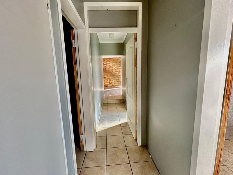 A functional hallway featuring tiled flooring and connecting multiple rooms, showing signs of wear on the walls and door frames.