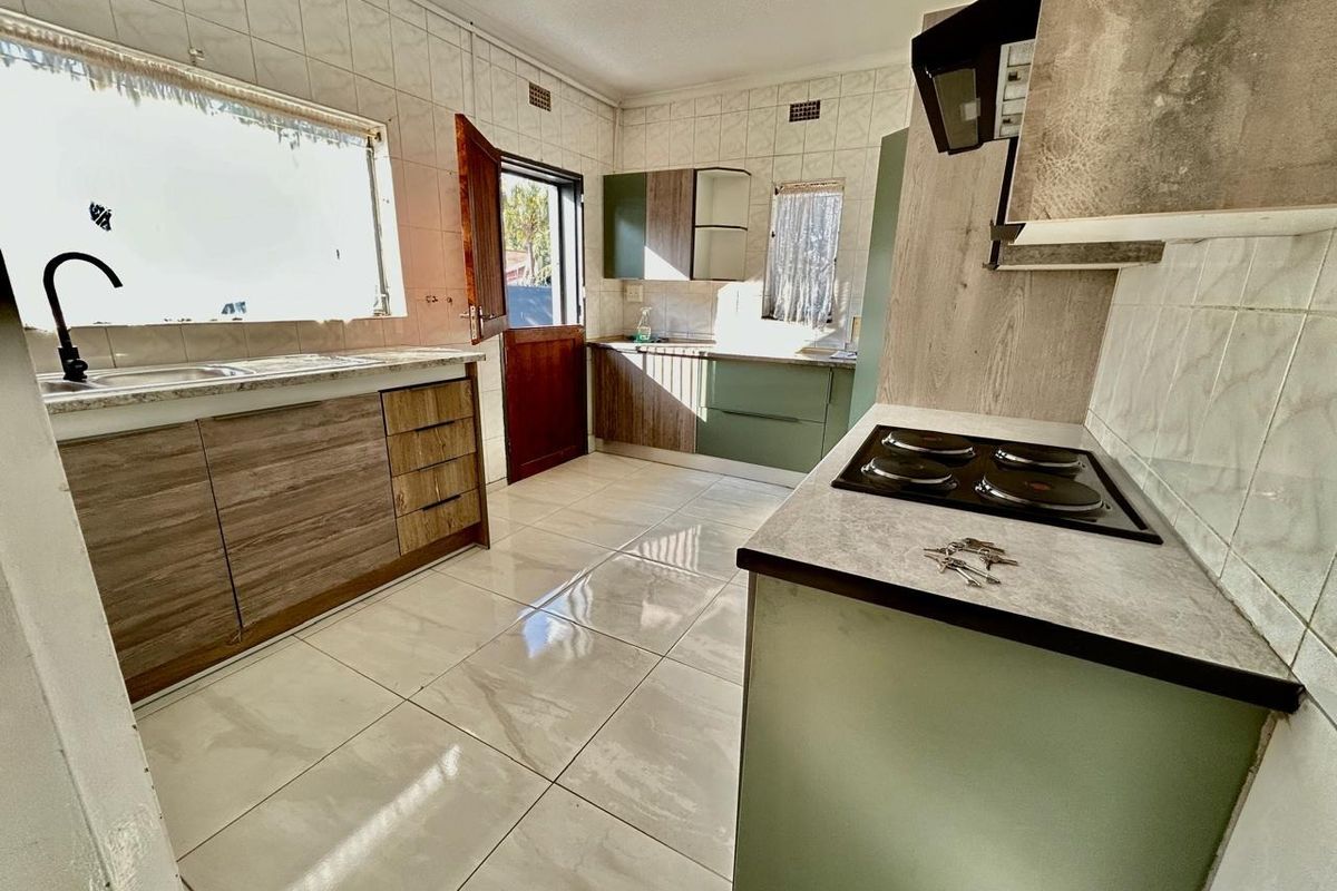 A functional kitchen featuring built-in cabinetry, laminate countertops, an electric hob with extractor fan, and tiled flooring throughout.