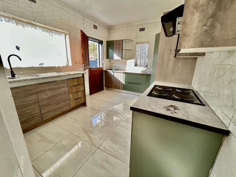 A functional kitchen featuring built-in cabinetry, laminate countertops, an electric hob with extractor fan, and tiled flooring throughout.