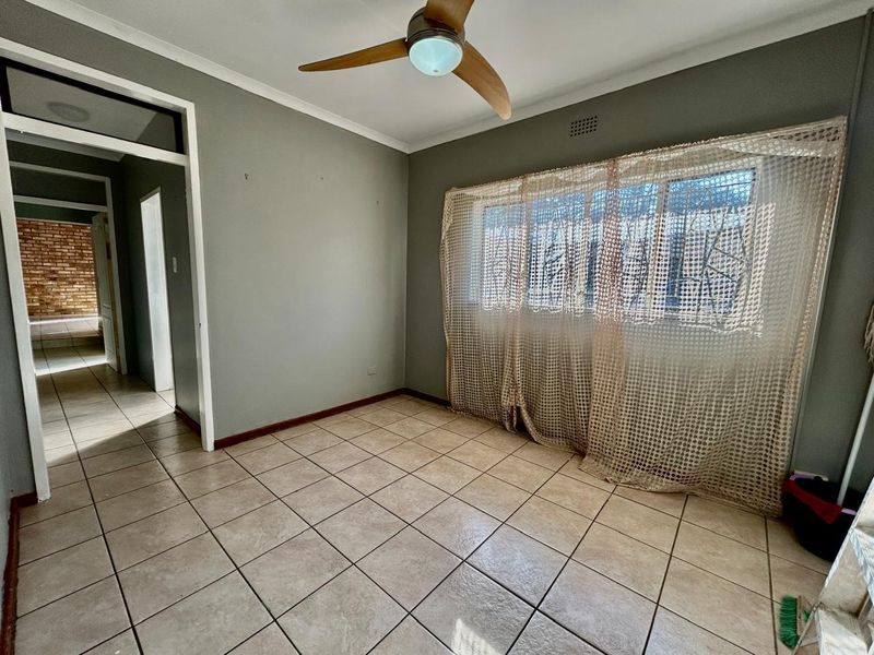 An empty bedroom featuring neutral grey walls, tiled flooring, and a ceiling fan, offering a blank canvas for personalization.