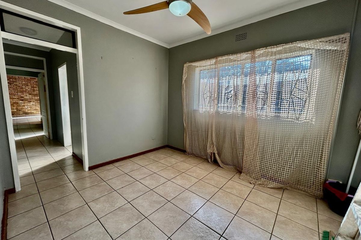 An empty bedroom featuring neutral grey walls, tiled flooring, and a ceiling fan, offering a blank canvas for personalization.