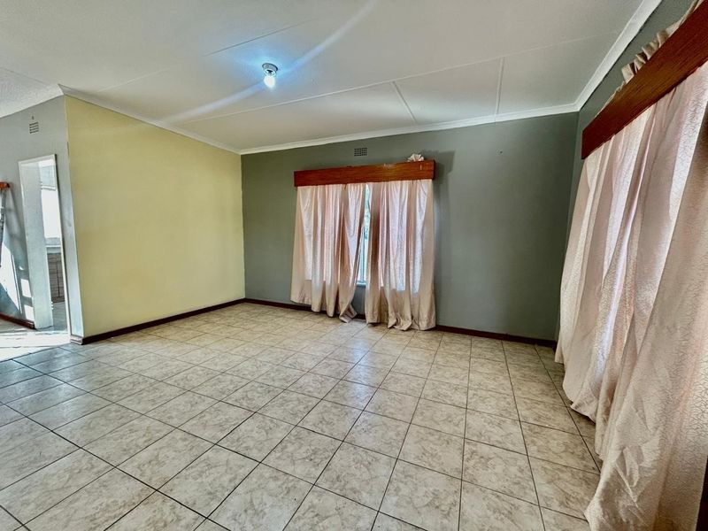 A spacious, empty living area featuring neutral tiled flooring and timber curtain pelmets, offering a blank canvas for interior design.