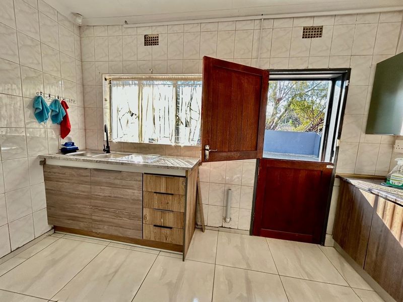 A functional kitchen area featuring tiled walls, laminate cabinetry, a double sink, and direct access to the exterior via a timber door.