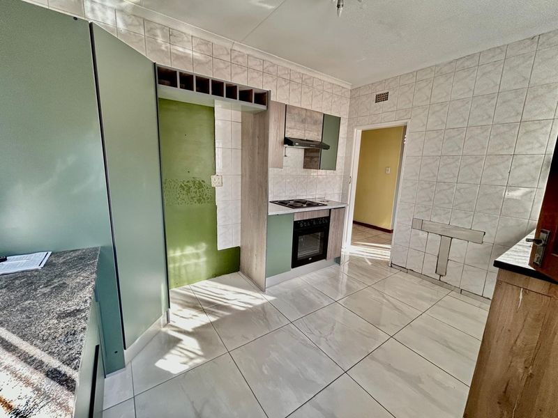 A kitchen space featuring tiled flooring and walls, built-in oven, hob, and extractor fan, currently requiring finishing touches to the wall surfaces.