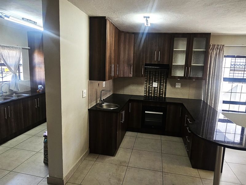 Spacious open-plan kitchen featuring dark wood cabinetry, black granite countertops, built-in oven, and a breakfast bar, with an adjacent scullery area.